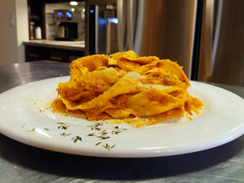 Pappardelle with marinara sauce on white plate, side shot with kitchen in background