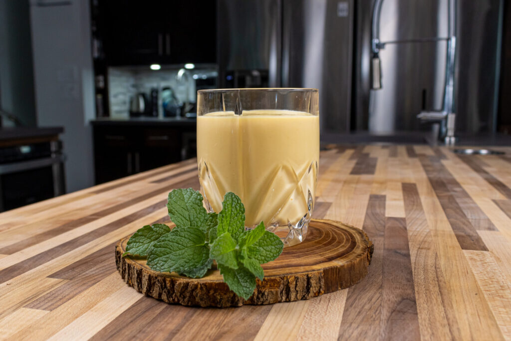 Czech egg liqueur (Czech Eggnog) in the glass on the wooden cutting board with mint leaves on the countertop.