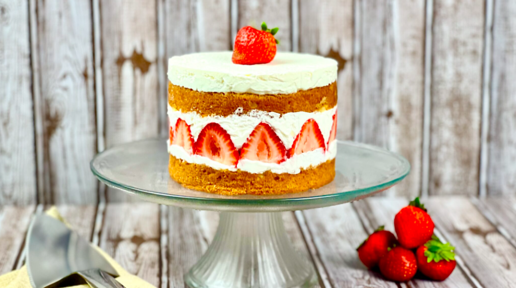 Strawberry Cream Cake on the cake stand, gray countertop, and background, fresh strawberries on the side.