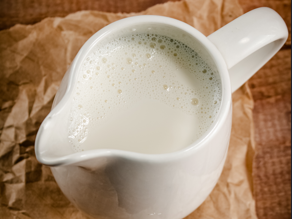 A small jug of butter milk on wooden background, top view