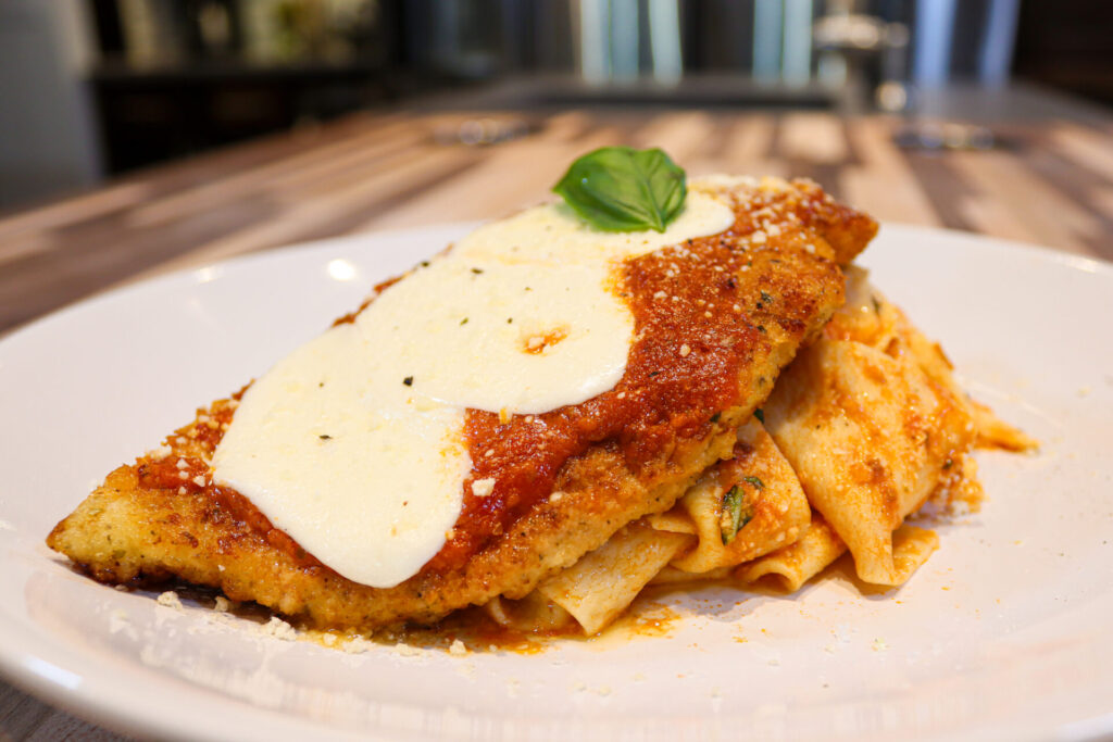 Chicken Parmesan with pappardelle on the white plate side shot from close distance with a little bit of kithen in the background