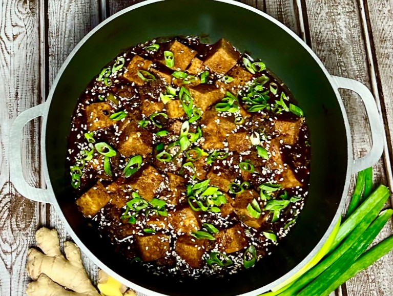 Easy Mapo Tofu in detail while still in the pan, on the rustic table surrounded with green onion and fresh ginger