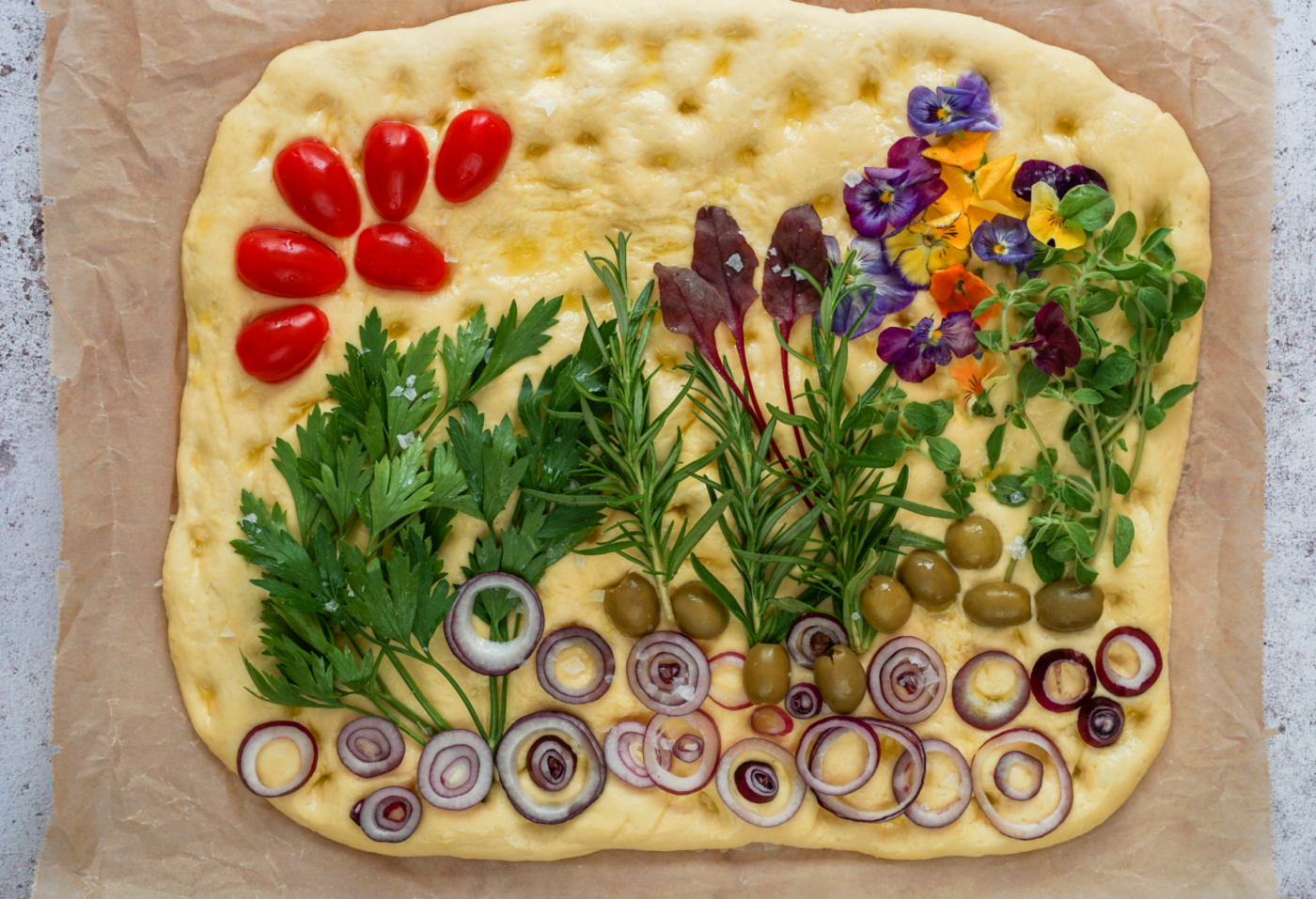 Decorated focaccia bread ready to be baked. Decorated with baby tomatoes, olives, red onions, and herbs. Top view.