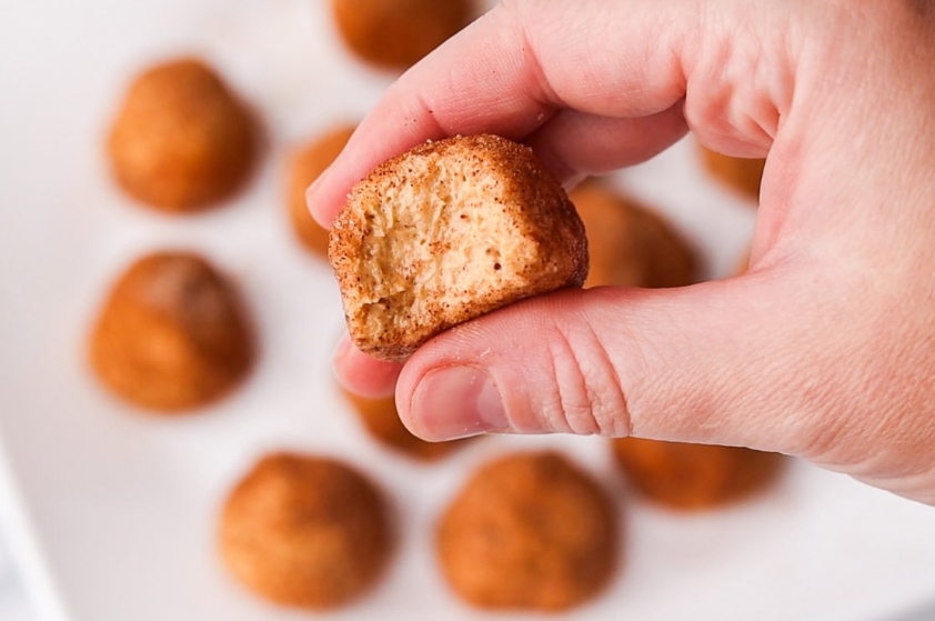 Keto No-Bake Pumpkin Pie Cheesecake Bites on the plate, above hand holding one of them with part bitten off