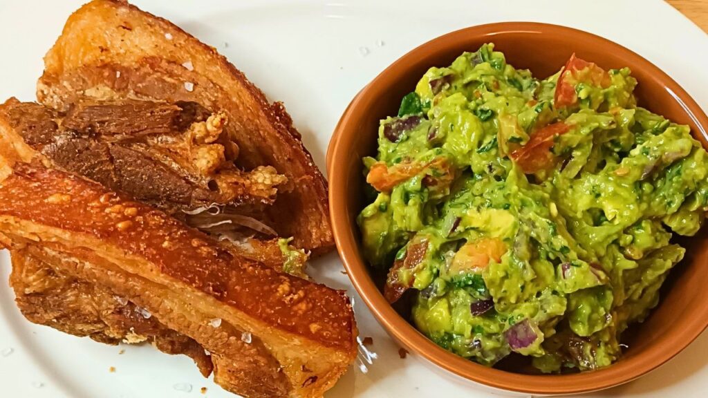 Pork Belly Chicharrones on the plate with Guacamole in the bowl, top close up view